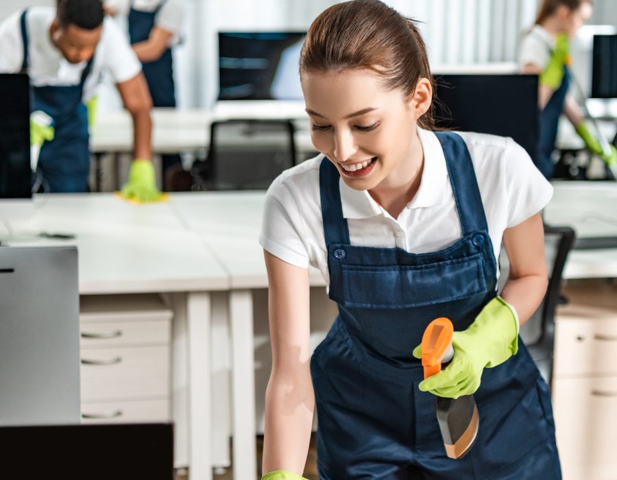 cheerful-cleaner-in-overalls-cleaning-office-desk-with-rag.jpg